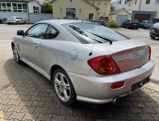Silver Hyundai Coupé GK in stock condition, rear three-quarter view in a car park